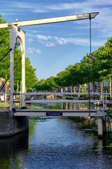 Weesp, Netherlands - July 05. 2022.  Groenebrug white drawbidge over the tree-lined Oude gracht  canal in the town centre against a blue sky.