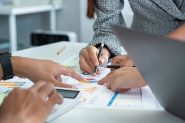 A team of businessmen plan with their laptops and graph charts for their profits and use a calculator to calculate their company's annual balance.