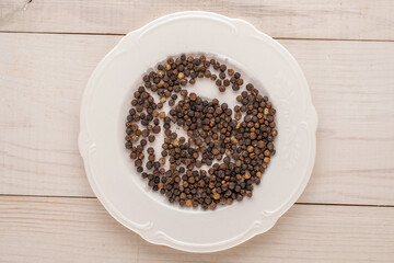 Dry fragrant black pepper with a ceramic dish on a wooden table, close-up, top view.