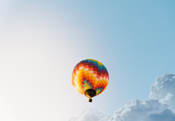 A very colorful hot air balloon flying next to a blue sky with perfect light and some clouds at the European hot air balloon festival.