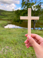 Women hand holding wooden cross. With nature background. Christianity concept.

