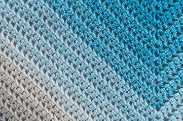 Fototapeta premium Crochet product from multicolored threads. Handmade backdrop. Fragment of a baktus of blue and white and grey tone. Striped and geometric pattern.