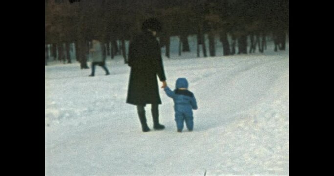 mother and child walking in winter snowy park. Mom holds kid by hand. People dressed in warm clothes. Family walks in cold forest. Lifestyle outdoors. Vintage color film. Family archive. Retro 1990s