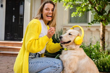woman in yellow sweater walking at her house with a dog listening to music in headphones