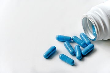 Blue capsules from a white pill jar on a white background.
