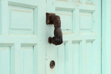 Turquoise wooden door has a rusty Hamsa or hand of Fatima shape Door knocker on it. Beautiful entrance to the house, vintage decoration. High quality photo