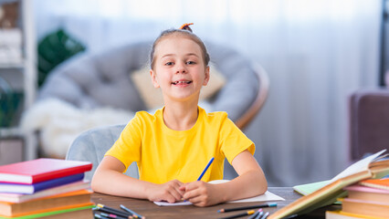 pretty happy schoolgirl is sitting at her desk at home and writing in a notebook. Preparation of homework. Back to school. little girl is happy to get knowledge and do her homework. Family education