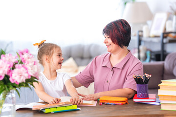 Happy mother and daughter write and read at home at the table. A modern woman and a little girl are happy to do their homework together. Rest time. Family education. Back to school