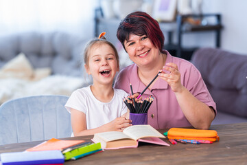 Happy mother and daughter write and read at home at the table. A modern woman and a little girl are happy to do their homework together. Rest time. Family education. Back to school