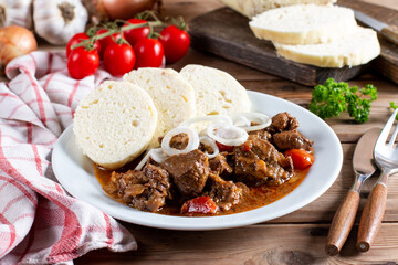 Czech traditional goulash with breaded dumpling and onion on white plate on table