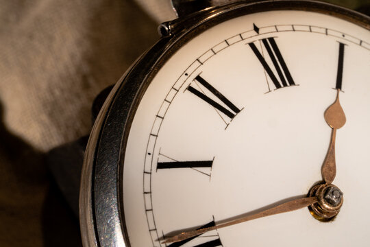 The dial face of an antique silver pocket watch with hands and Roman numerals. Close up of a round retro watch with a white dial. Luxury aged timepiece. Mechanical old metal clock.