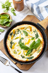 Spinach and cheese omelette. Frittata made of eggs, paprika and spinach in a frying pan on a marble countertop.
