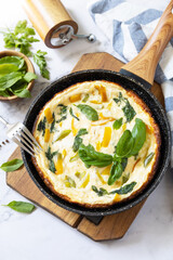 Spinach and cheese omelette. Frittata made of eggs, paprika and spinach in a frying pan on a marble countertop. Copy space.