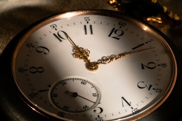 The white dial face of an antique round pocket watch with hands and numbers. Close up of a black and gold retro watch with golden hands. Luxury aged timepiece. Mechanical old metal clock.