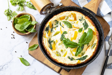 Spinach and cheese omelette. Frittata made of eggs, paprika and spinach in a frying pan on a marble countertop. Copy space.
