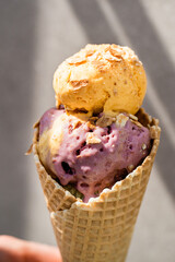 Melting vanilla ice cream with pink and yellow scoops in a waffle cone close-up