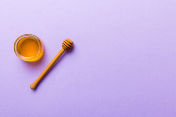 Glass jar of honey with wooden drizzler on colored background. Honey pot and dipper high above. Top view copy space