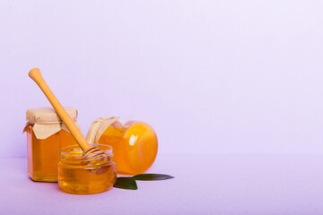 Honey in jar with leaves and honey dipper on colored background top view with copy text