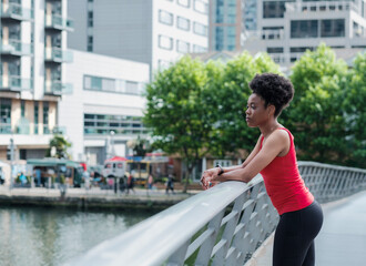 A black sport young woman is looking away leaning on a banister bridge.