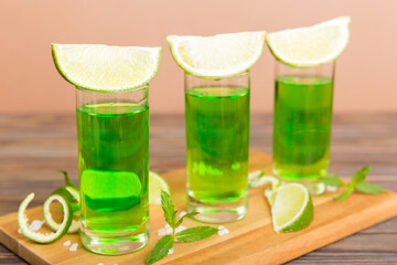 Sweet refreshing mint liqueur, with ice and mint leaves on table background, Shots with lime slice and mint flat lay