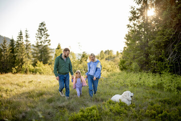 Young caucasian couple with little girl and dog walk together while traveling in the mountains. Happy family spending summer vacation on nature