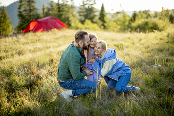 Portrait of a lovely couple with little girl hug together while travel in the mountains. Young caucasian family spend summer time on nature