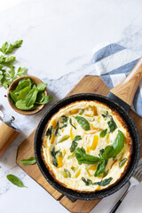 Spinach and cheese omelette. Frittata made of eggs, paprika and spinach in a frying pan on a marble countertop. View from above. Copy space.