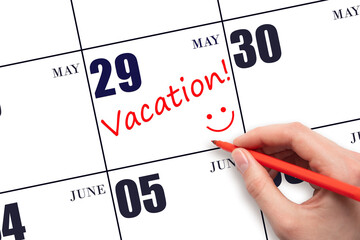 A hand writing a VACATION text and drawing a smiling face on a calendar date 29 May. Vacation planning concept.