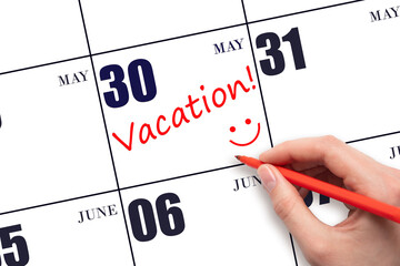 A hand writing a VACATION text and drawing a smiling face on a calendar date 30 May. Vacation...