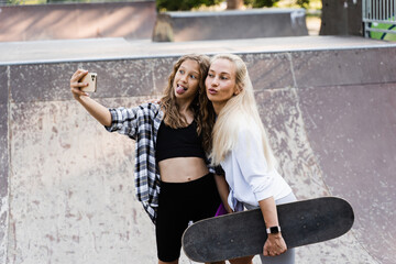 Mother and child daughter with skate and penny board is making selfie on phone in skate park....