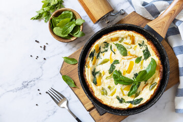 Spinach and cheese omelette. Frittata made of eggs, paprika and spinach in a frying pan on a marble countertop. View from above. Copy space.