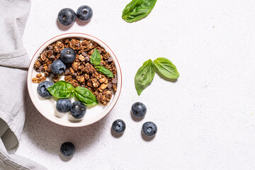 Homemade granola with yogurt and blueberries on the marble tray on white stone background top view. Healthy tasty breakfast concept.