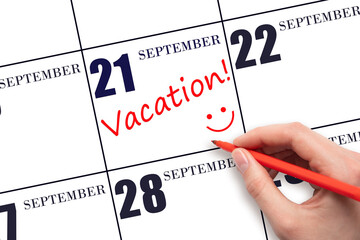 A hand writing a VACATION text and drawing a smiling face on a calendar date 21 September . Vacation planning concept.