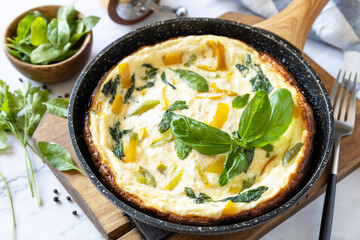 Spinach and cheese omelette. Frittata made of eggs, paprika and spinach in a frying pan on a marble countertop.