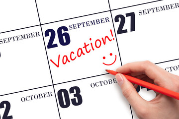 A hand writing a VACATION text and drawing a smiling face on a calendar date 26 September . Vacation planning concept.