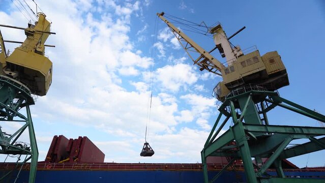 Grain transshipment from container to ship cargo holds with a double rope dual scoop clamshell grab on crane in sea port. Wheat shipment with water transport. Agricultural commodities transportation.