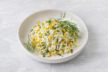 White ceramic bowl with vegetarian cabbage salad with corn, eggs, herbs, mayonnaise on a light gray background
