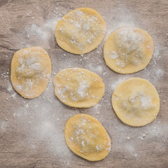 Uncooked stuffed raviolonis or raviolis with flour with ingredients over wooden table