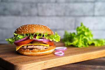 hamburger with cutlet, tomato, cheese and lettuce leaves on a wooden board