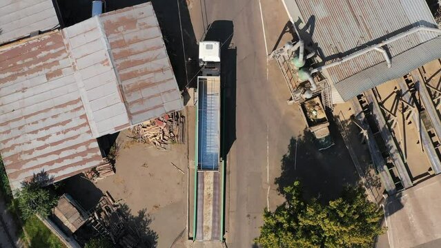 Aerial view from above of grain lorry or dump truck driving through the industrial area of grain elevator silos. Top view of emty body trailer driving along the road. Air drone copter footage.