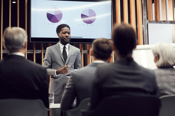 Content confident young Afro-American financial specialist in gray suit standing against plasma...