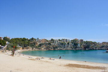 Fototapeta na wymiar Porto Cristo, Mallorca, Spain - 05.02.2022: Half empy beach of Porto Cristo with houses on top of the coastal cliffs in background