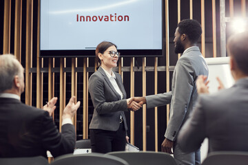 Happy excited young businesswoman in glasses making handshake with investor after obtaining...