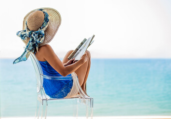 detail view of a woman in a hat sitting on the terrace of a hotel looking at the sea with a magazine in her hand. concept vacation on the spanish coast.