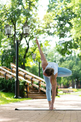 Young man practice yoga in the park. Yoga asanas in city park, sunny day. Concept of meditation,...