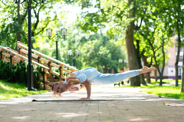 Young man practice yoga in the park. Yoga asanas in city park, sunny day. Concept of meditation,...