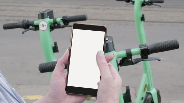 A woman orders electric scooters through her smartphone, ride sharing. Hand with phone with empty screen.