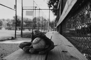 Old used baseball equipment on field dugout bench in black and white closeup. - Powered by Adobe