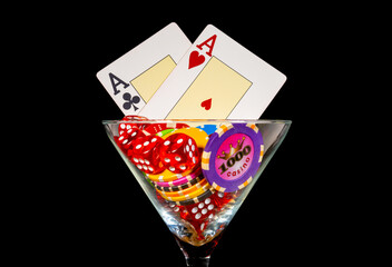 Cards, set of dice and casino chips in martini glass on black isolated background. Two aces, chip denominated in one thousand and red dice. Gambling background, poker, roulette, bridge. Extra close up