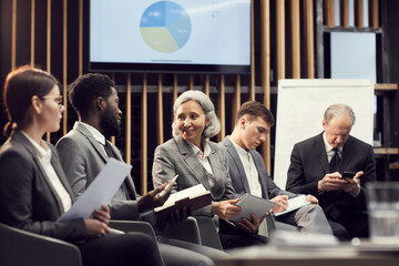 Smiling Asian lady and Afro-American man sitting in board room and discussing statistics at...
